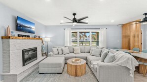 Ein modernes Wohnzimmer mit einem Ecksofa, einem Kamin, einem runden Couchtisch aus Holz und einem Deckenventilator.