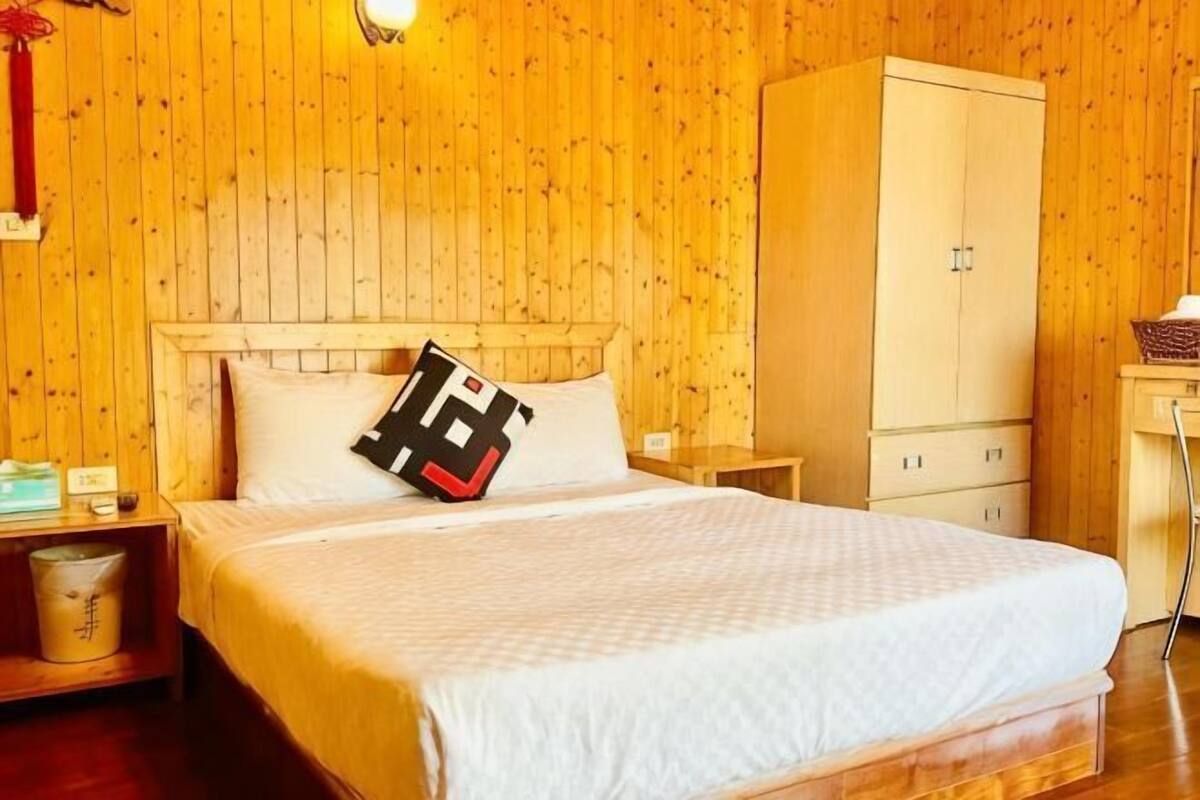 A wooden-paneled room with a bed, nightstands, a wardrobe, and a desk.