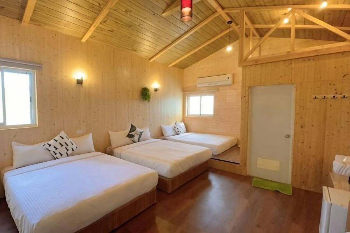 A wooden cabin with two beds, a window, a door, and a ceiling with exposed beams.