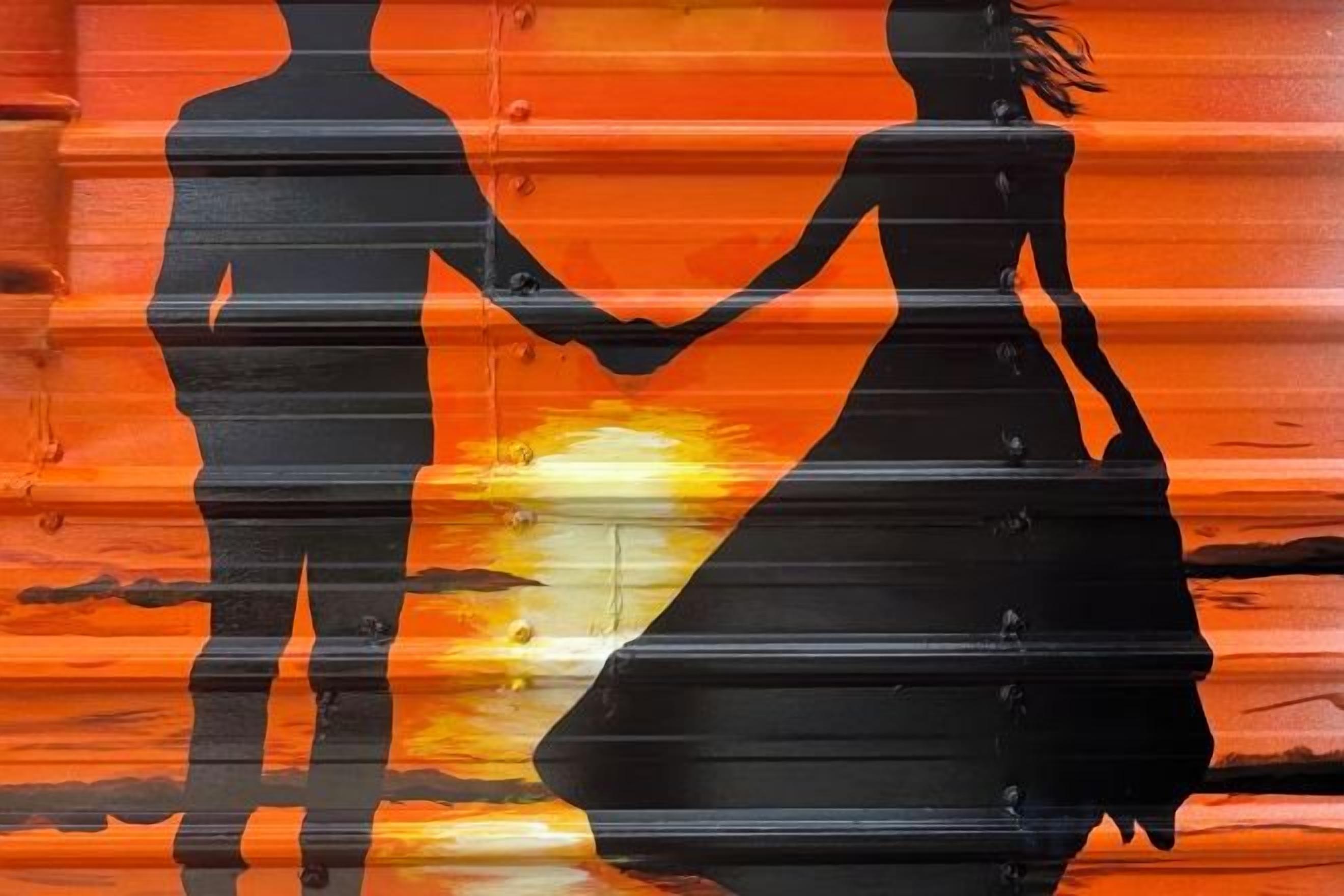 La silhouette d’un couple se tenant la main, se détachant sur le fond d’un coucher de soleil.