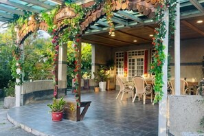 A covered outdoor seating area with a wooden arch, potted plants, and a dining table with chairs. - Quiet Home Hall (Pingtung)