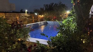 Una piscina esterna circondata da vegetazione lussureggiante e luci decorative.