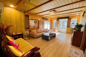 A spacious living room with wooden flooring, a sofa, a coffee table, and a fan. - Quiet Home Hall (Pingtung)