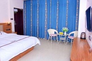 A hotel room with a bed, a desk, a chair, a table with flowers, and a TV.
