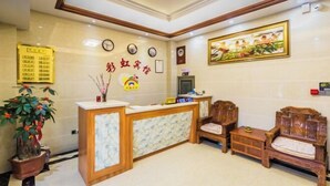 A reception area with a wooden reception desk, two wooden chairs, a potted plant, and a wall-mounted clock. - Weizhou Island Rainbow Hotel (Putian)
