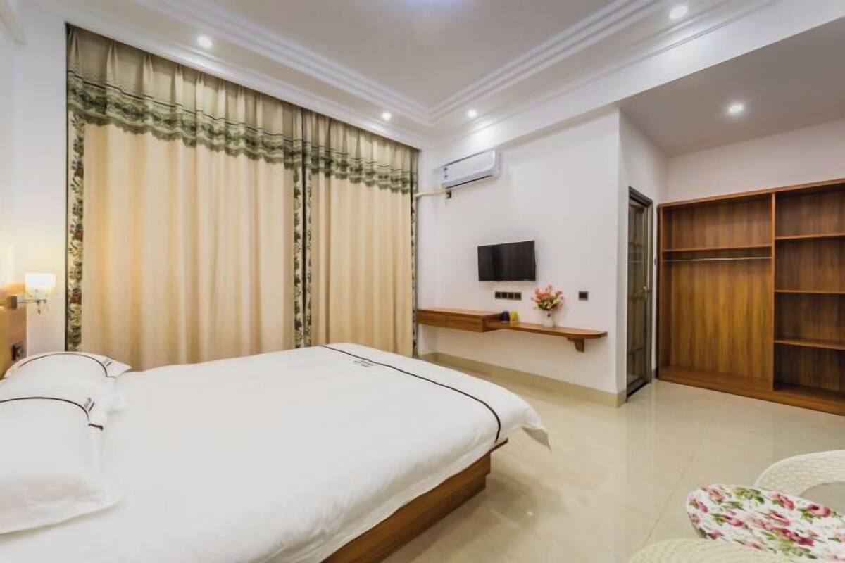 Een hotelkamer met een bed, een televisie, een kledingkast en een klein plankje met een bloevas.