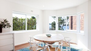 Un comedor con una mesa redonda, sillas blancas y vistas a la vegetación y al agua a través de amplias ventanas.