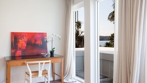 Una habitación con un escritorio de madera, una silla blanca, un cuadro abstracto rojo, una orquídea blanca y vistas a una masa de agua a través de una puerta de cristal.