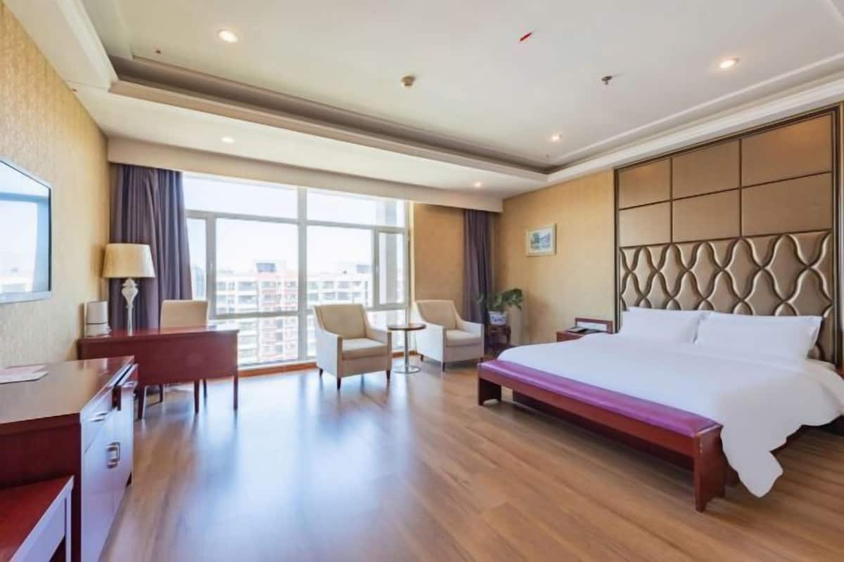 Une chambre d’hôtel avec un grand lit, un bureau, deux chaises, une petite table et une vue sur la ville.