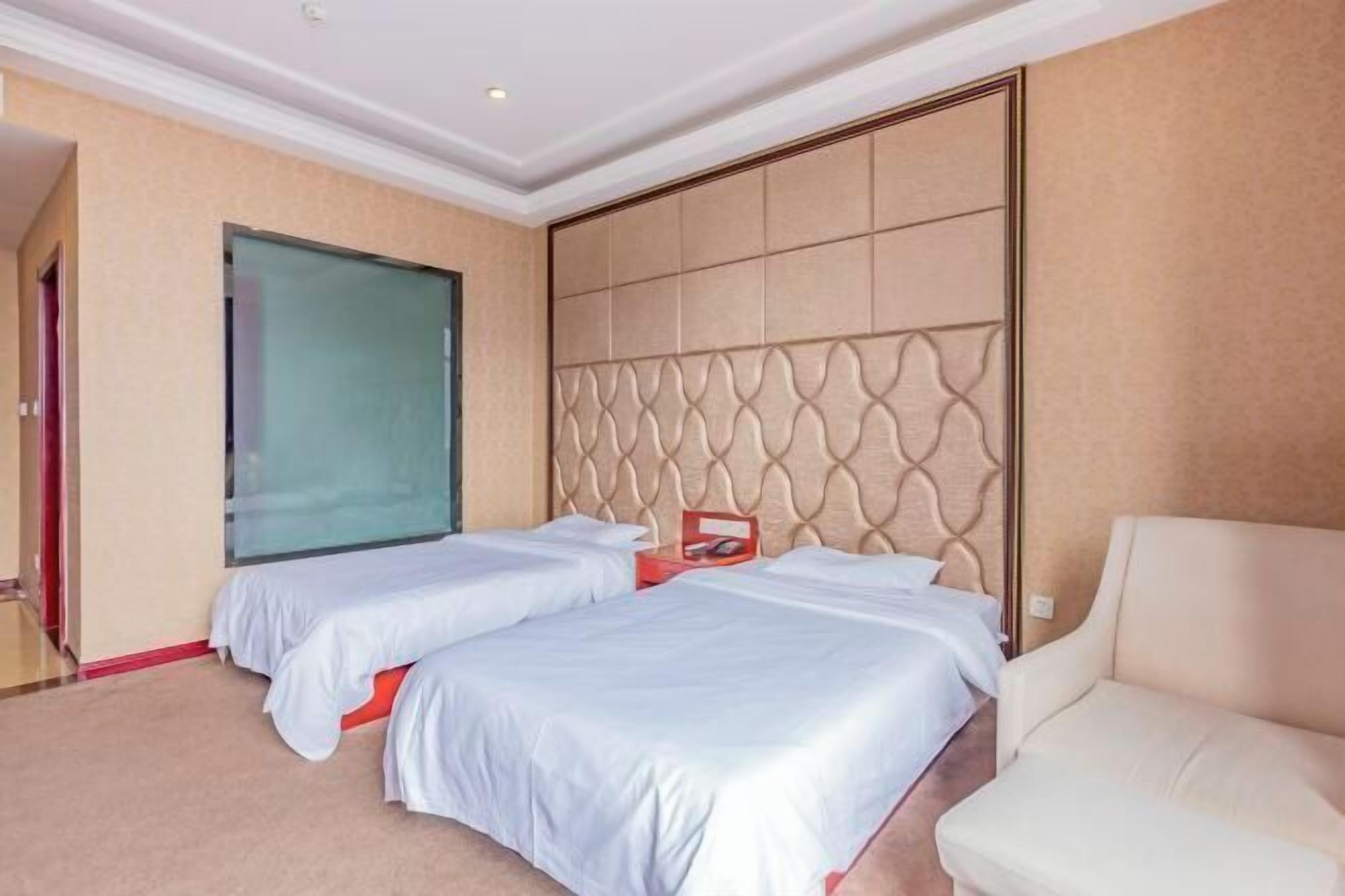 Une chambre d’hôtel avec deux lits, une grande fenêtre, une tête de lit rembourrée et un fauteuil blanc.
