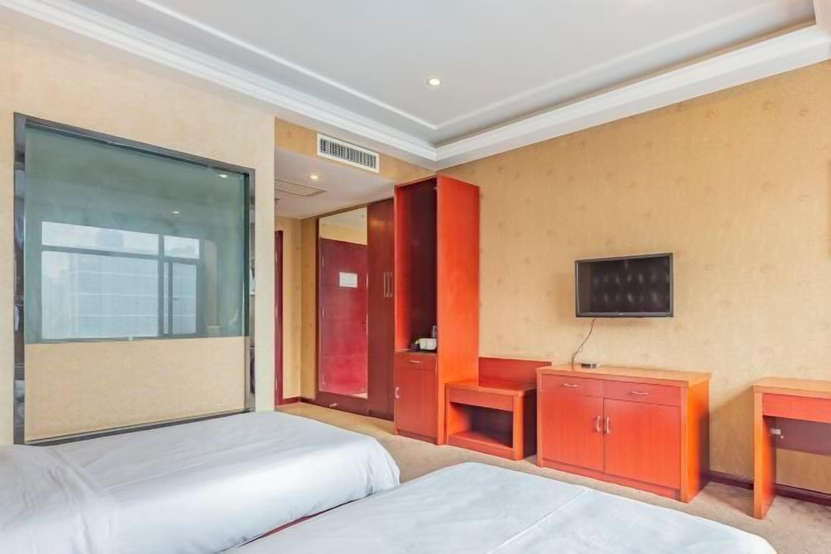 Ein Hotelzimmer mit zwei Betten, einem Fernseher, einem Kleiderschrank und einem Schreibtisch.