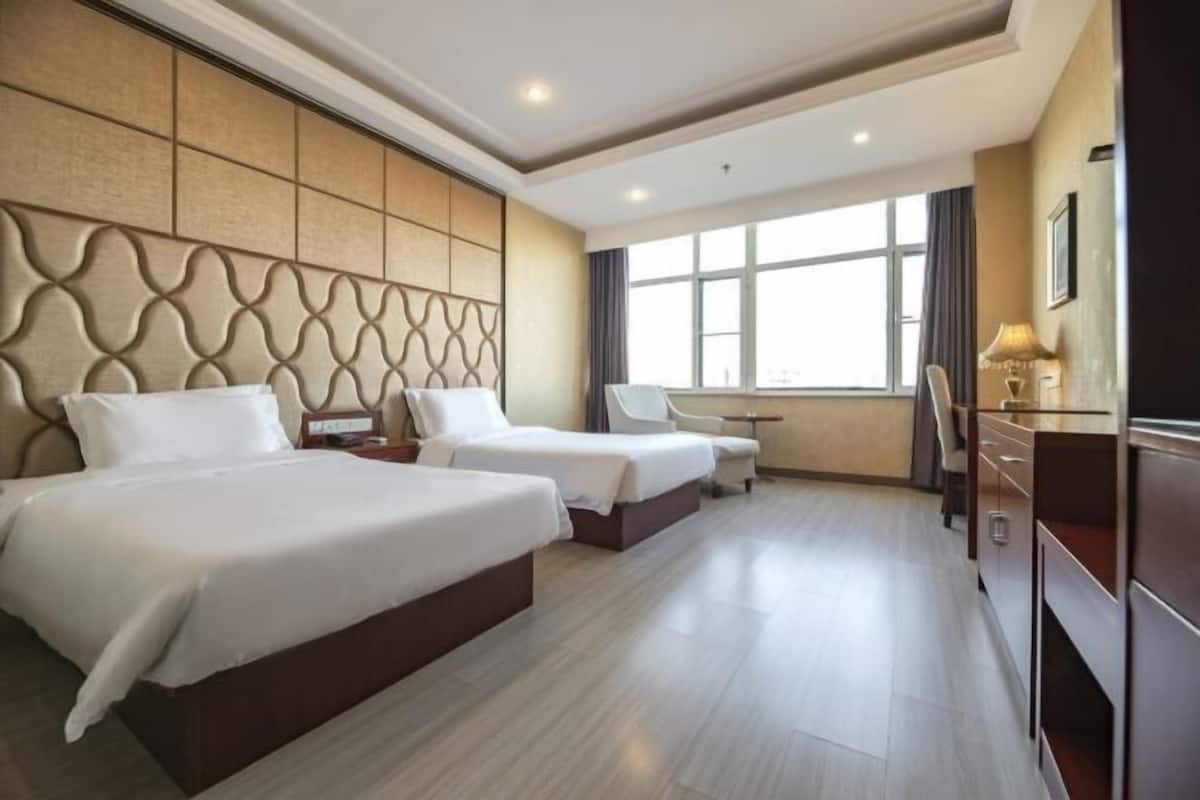 Une chambre d’hôtel avec deux lits, un bureau, une chaise et une grande fenêtre.