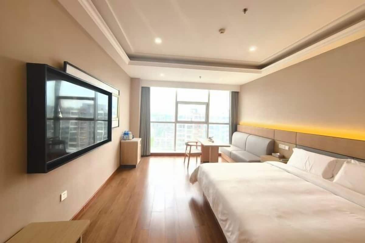 Une chambre d’hôtel équipée d’un lit, d’un bureau, d’une chaise, d’un téléviseur fixé au mur et d’une fenêtre donnant sur la ville.