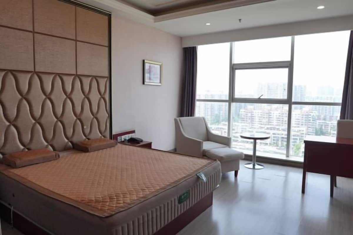 Une chambre d’hôtel avec un grand lit, une chaise, une petite table et une vue sur la ville grâce à de grandes fenêtres.