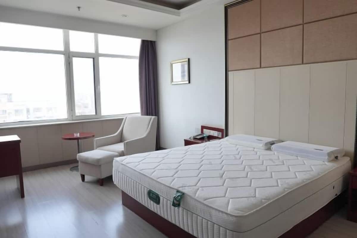 Une chambre d’hôtel avec un grand lit, une chaise, une petite table et une fenêtre.