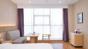 A hotel room with a bed, a sofa, a small table, a chair, a desk, a cabinet, and a large window with curtains. - Henghui Hyatt Hotel (Shijiazhuang)