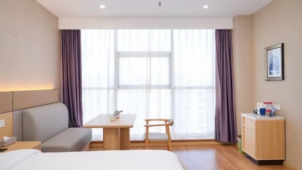 A hotel room with a bed, a sofa, a small table, a chair, a desk, a cabinet, and a large window with curtains. - Henghui Hyatt Hotel (Shijiazhuang)