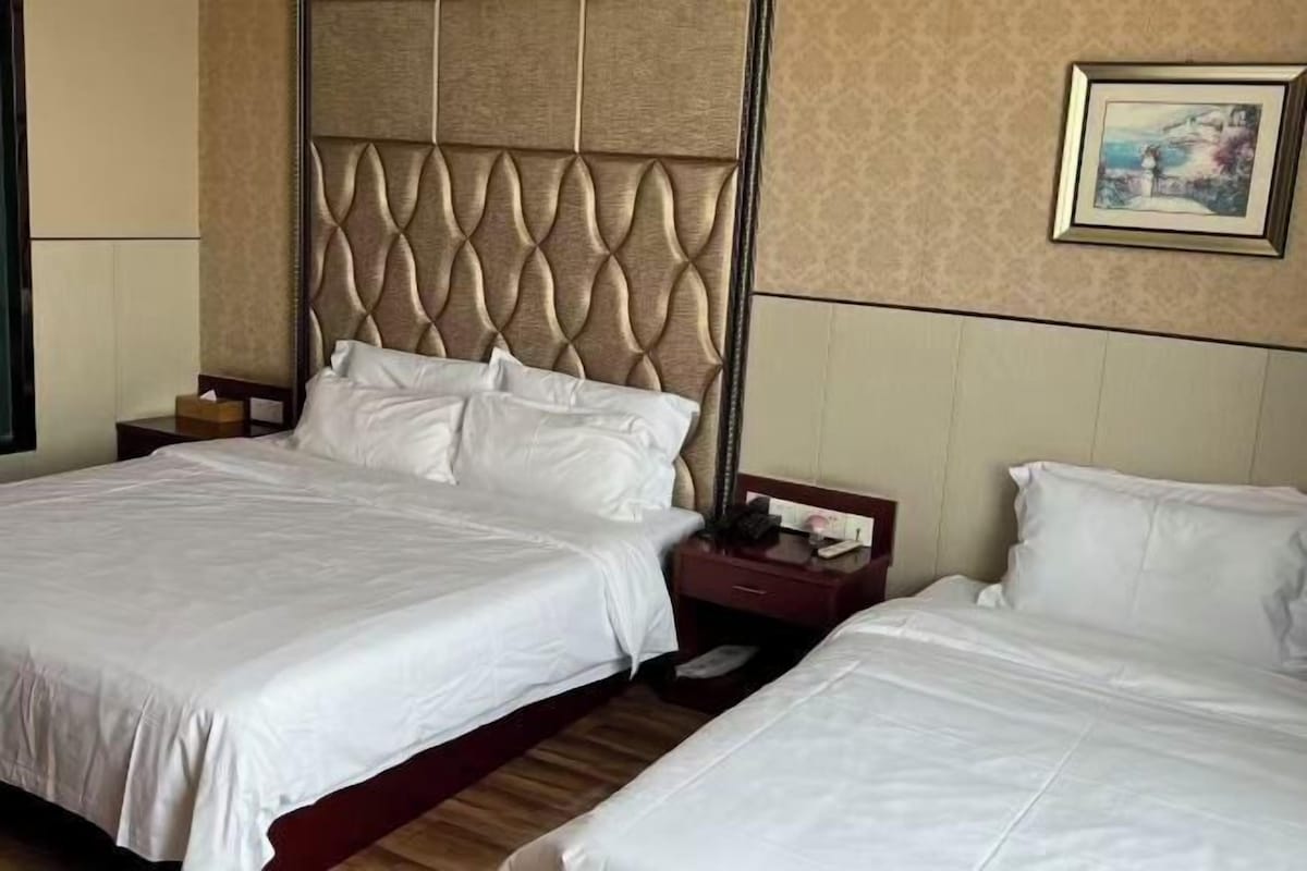 A hotel room with two beds, a padded headboard, a nightstand, and a framed picture on the wall.