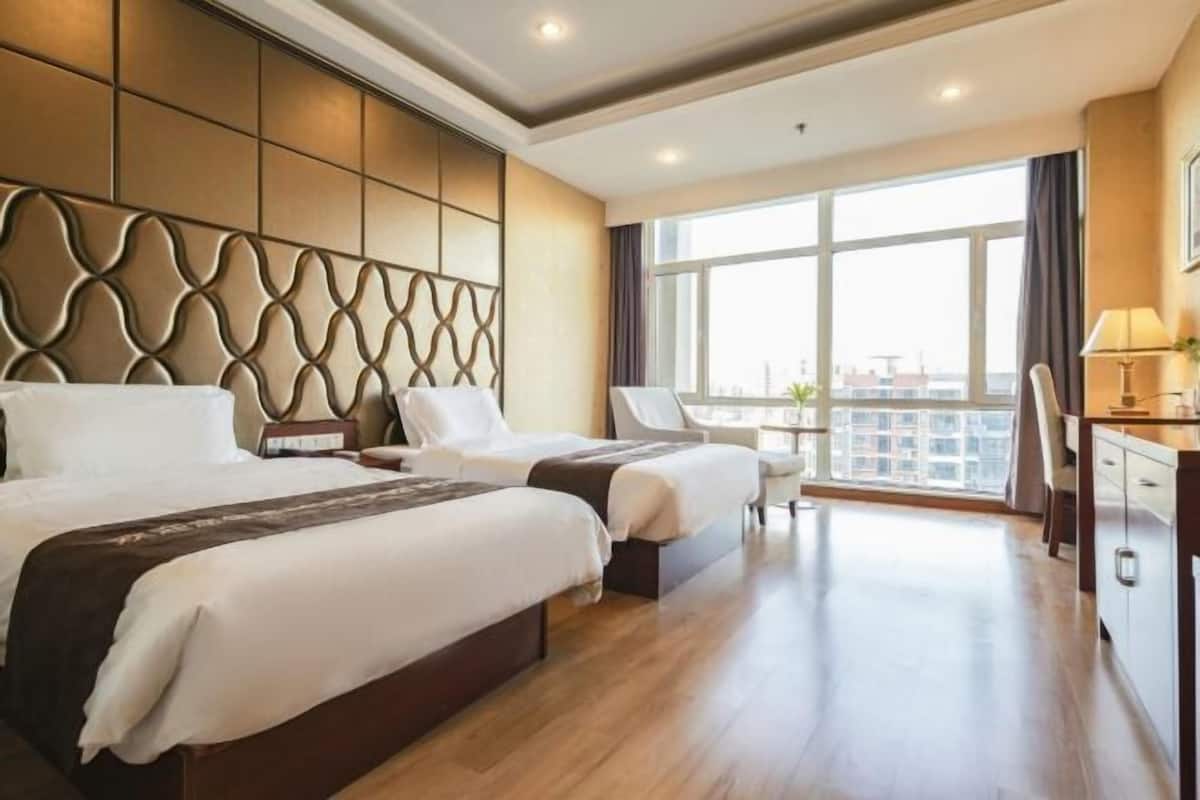 Une chambre d’hôtel avec deux lits, un bureau, une chaise et une grande fenêtre donnant sur la ville.