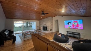 A living room with a stone fireplace, wooden ceiling, and a television displaying animated characters. - Lakefront Ranch with Hot Tub and WiFi in Crescent City (Crescent City)