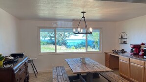 A kitchen with a wooden table and benches, a window with a view of greenery, and a hanging light fixture. - Lakefront Ranch with Hot Tub and WiFi in Crescent City (Crescent City)