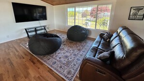 A living room with a wooden ceiling, a large TV, a brown leather sofa, two black bean bags, and a patterned rug. - Lakefront Ranch with Hot Tub and WiFi in Crescent City (Crescent City)