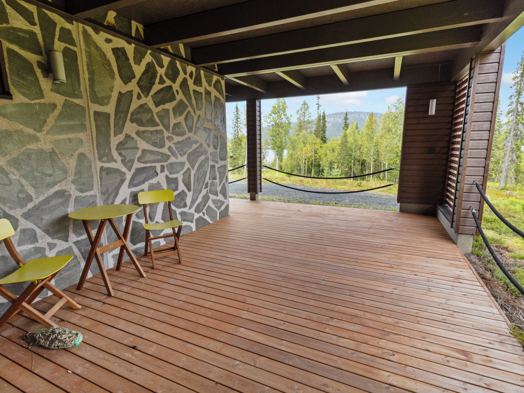 Een houten terras buiten, met stenen muren en uitzicht op een bos en bergen.