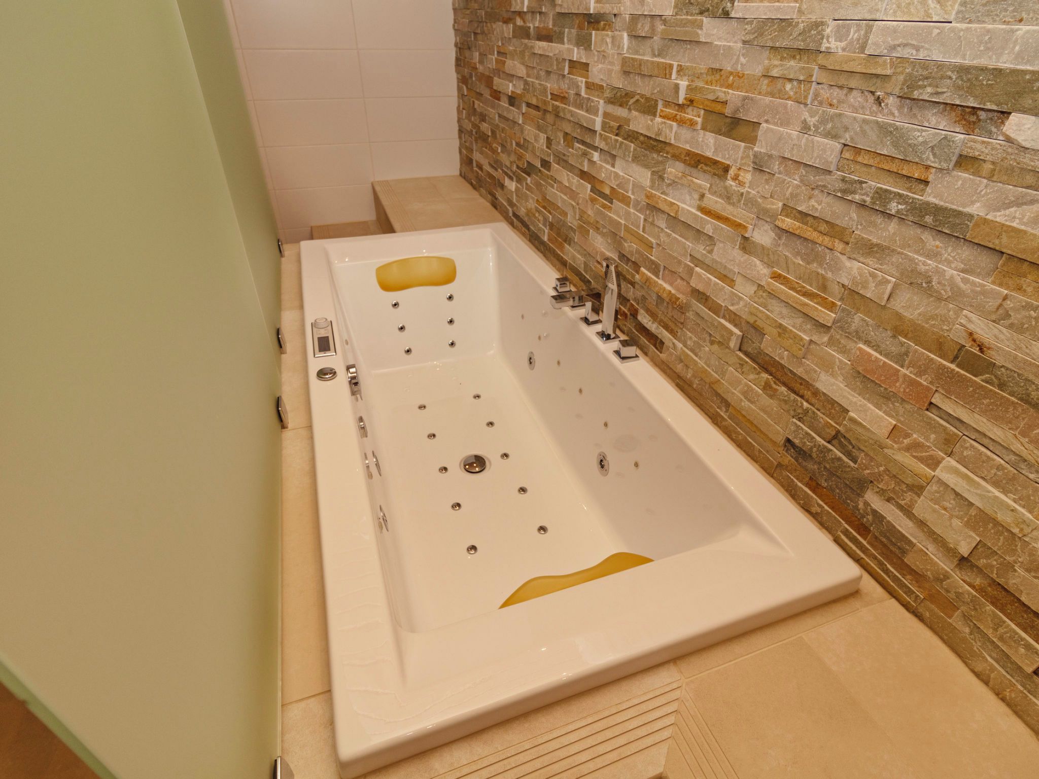 Une salle de bain avec une grande baignoire, une douche et un mur en pierre.