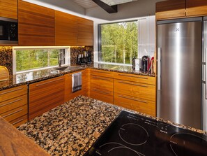 A modern kitchen with wooden cabinets, a granite countertop, a built-in oven, and a stainless steel refrigerator.