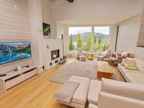 A modern living room with a fireplace, a television, and a large window offering a scenic view. - Holy lake chalet a by Interhome (Kuusamo)