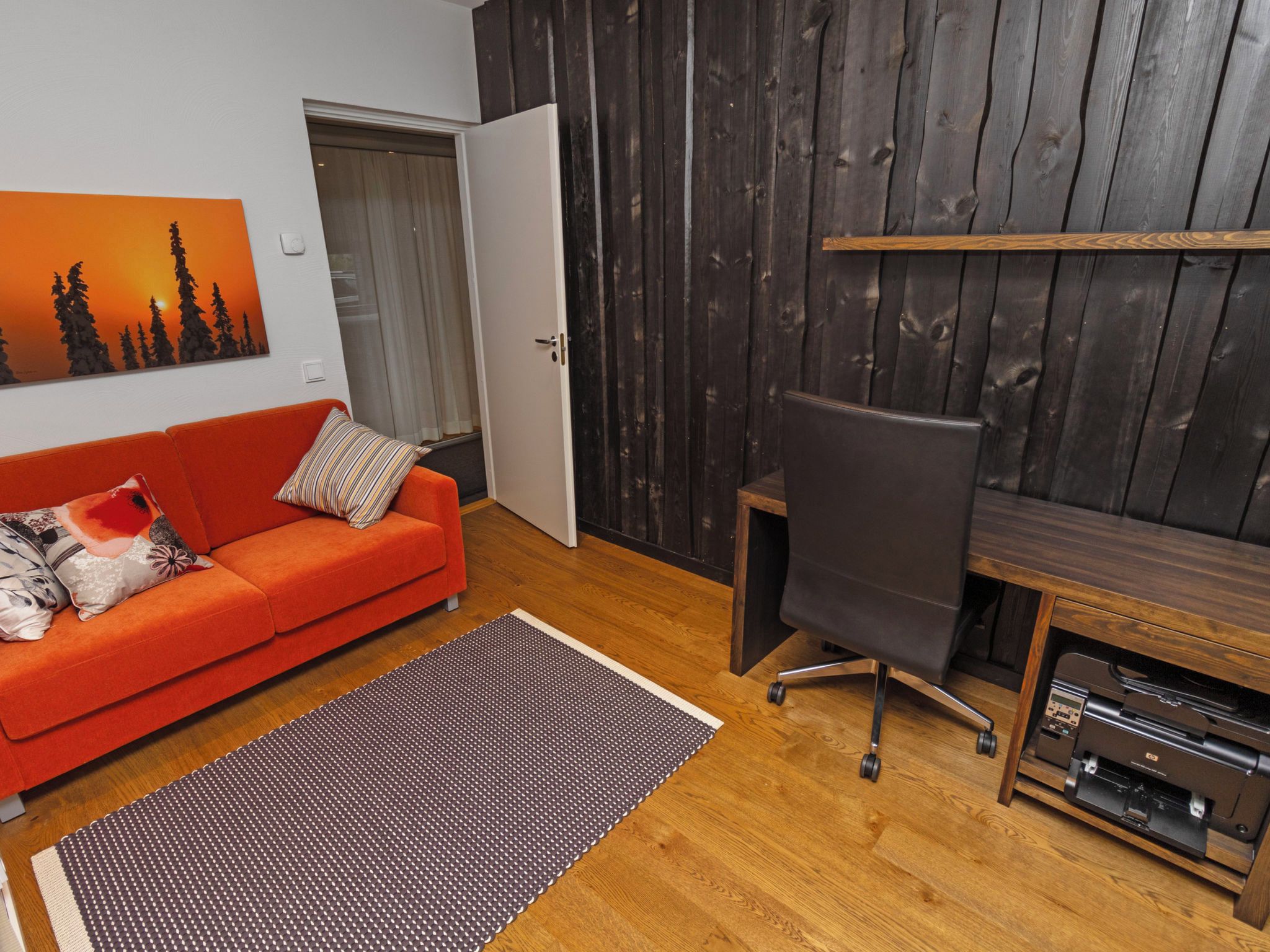 Ein Zimmer mit einer roten Couch, einem Holztisch und einem Drucker.