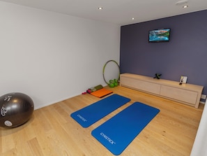 A room with a wooden floor, two blue exercise mats, a large exercise ball, a green yoga wheel, and a wall-mounted TV. - Holy lake chalet a by Interhome (Kuusamo)