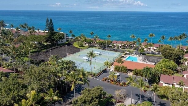 Vista aérea de un complejo turístico costero con cancha de tenis, piscina y vistas al océano.