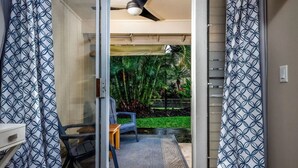 Una habitación con puerta de cristal corredera que da a un patio con una silla, una mesita y un ventilador de techo.