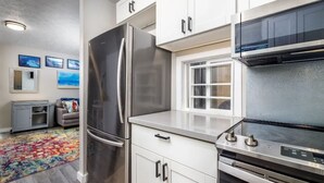 Una cocina moderna con electrodomésticos de acero inoxidable, armarios blancos y un ventanal que proporciona luz natural.
