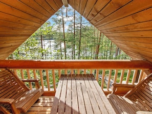 A wooden deck with a view of a forest and a body of water. - Karhupirtti by Interhome (Mäntyharju)