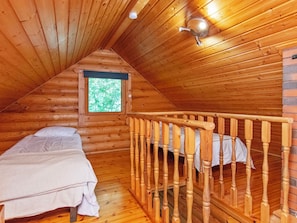 A cozy attic bedroom with wooden walls, a window with a view of trees, a bed, and a wooden railing. - Karhupirtti by Interhome (Mäntyharju)