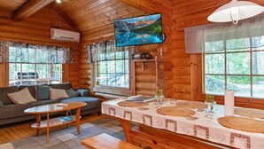 Interior acogedor de una cabaña de madera con un sofá, una mesa y un televisor montado en la pared.