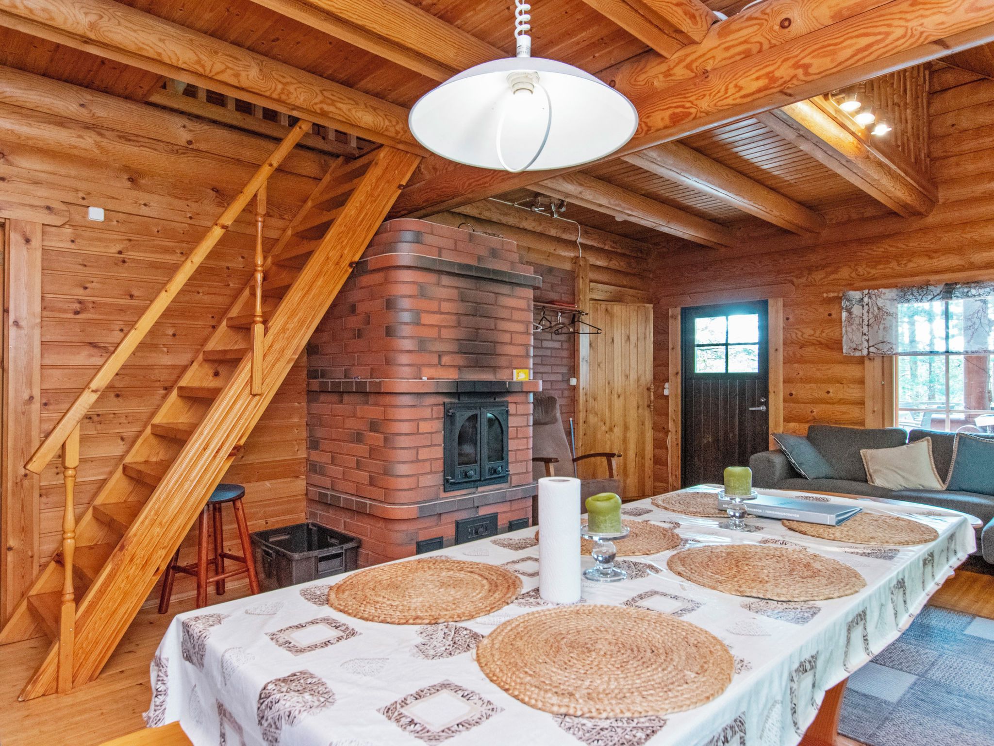 Et interiør i træ med en murstenspejs, et spisebord med servietter, en trappe og en sofa.