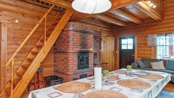 Et interiør i træ med en murstenspejs, et spisebord med servietter, en trappe og en sofa.