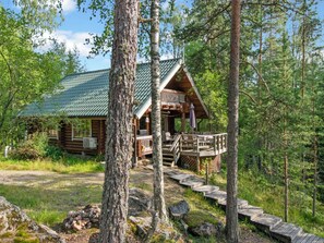 A log cabin with a porch and deck, surrounded by trees and a clear sky.