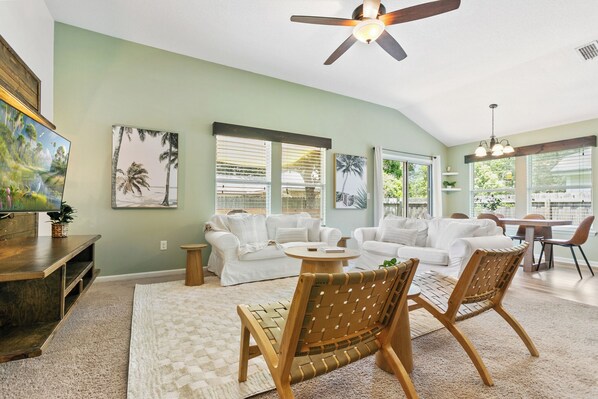 A spacious living room with a high ceiling, a ceiling fan, a dining area with a table and chairs, and large windows providing natural light. - Charming 3-bedroom house in Jacksonville (Jacksonville)