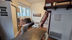 A compact living space with a sofa, a coffee table, and a dining table. A staircase leads to an upper level.