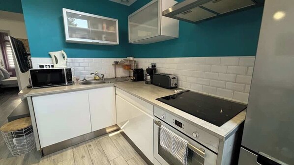 A modern kitchen with white cabinets, a black induction cooktop, a built-in oven, and a microwave.