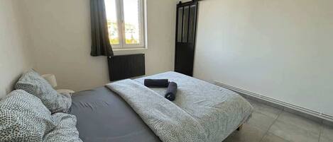 A bedroom with a bed, pillows, a window, and a radiator.