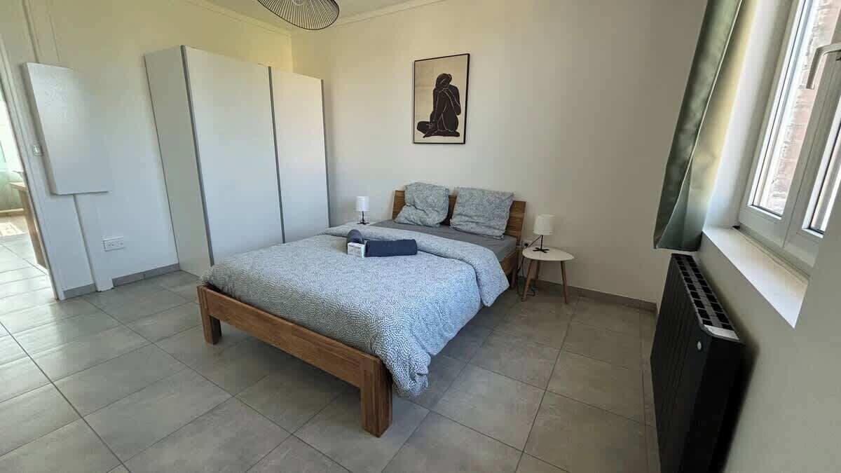 A bedroom with a bed, bedside tables, a radiator, and a window.