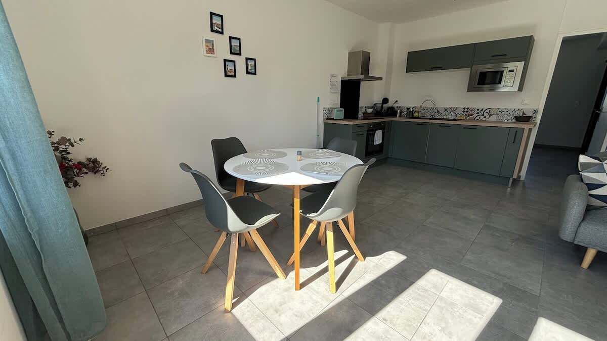 Een moderne keuken met een magnetron en kookplaat, een eethoek met een ronde tafel en stoelen, en een grijze bank.