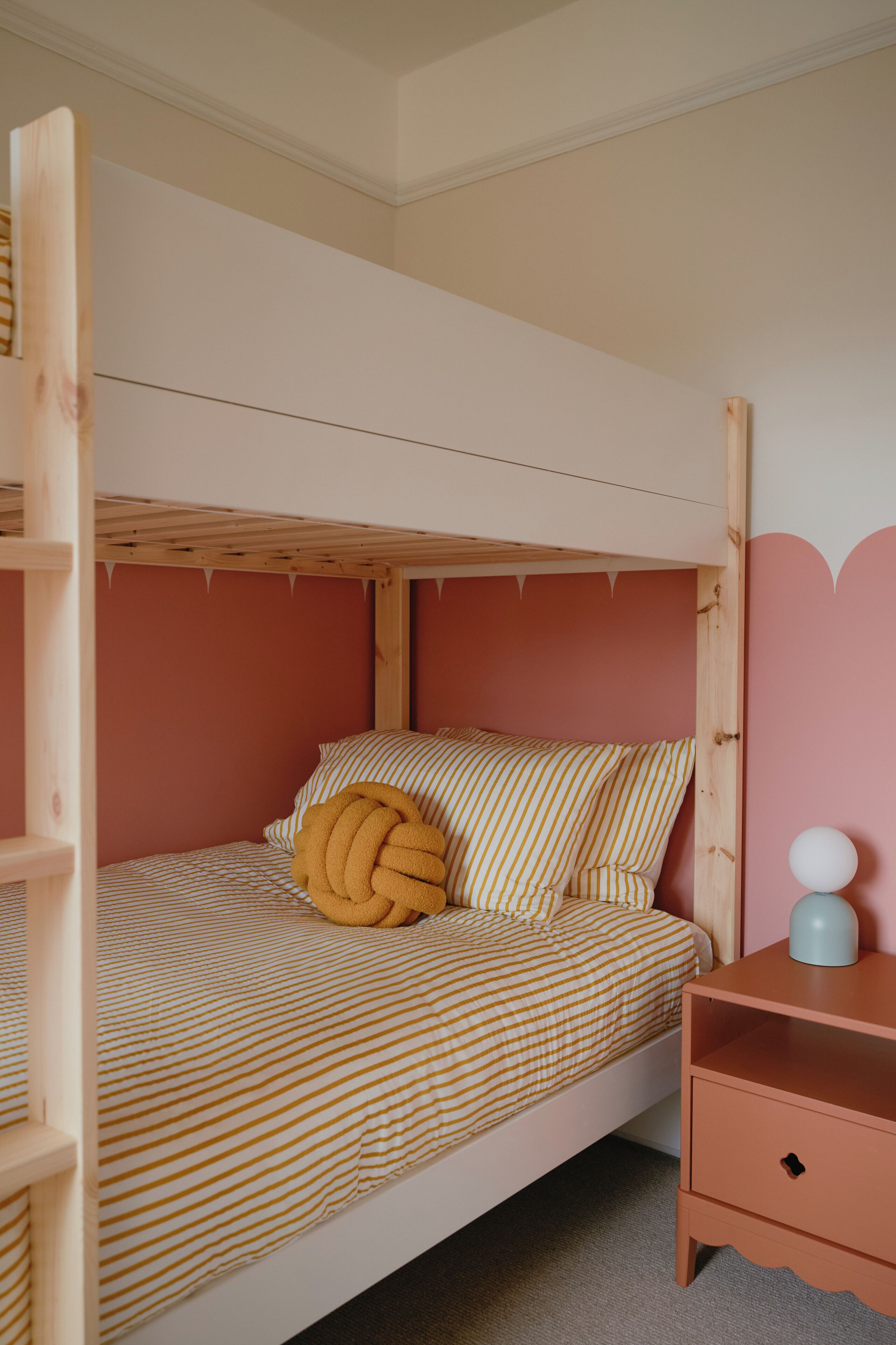 A bunk bed with striped bedding, a wooden headboard, and a pink wall.