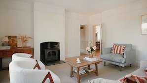 A living room with a fireplace, a coffee table, and a patterned armchair. - Trinity Farmhouse-Stunning House&Garden (Cirencester)