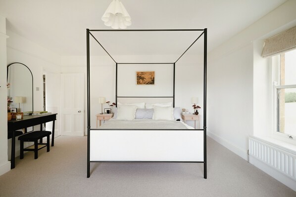 Un lit à baldaquin avec une couvre-lit rayée de blanc et de gris, une structure en métal noir et deux tables de chevet avec des lampes.